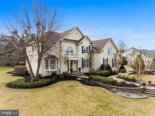 view of front of house with a front yard, a balcony, and stucco siding