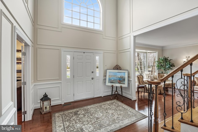 entryway featuring crown molding, dark wood-style flooring, a decorative wall, and stairs