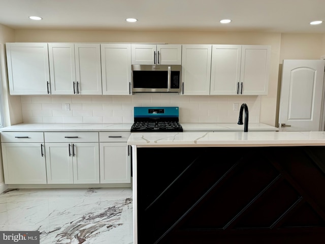 kitchen with light stone counters, marble finish floor, tasteful backsplash, stainless steel microwave, and gas range