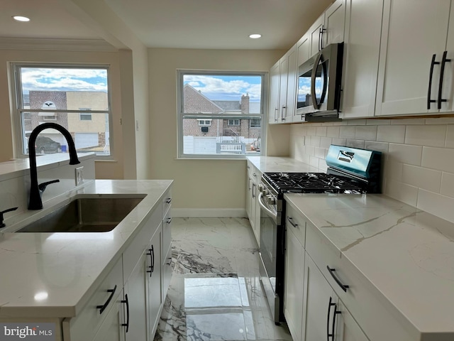 kitchen with a sink, baseboards, marble finish floor, appliances with stainless steel finishes, and tasteful backsplash