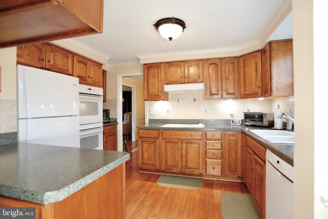 kitchen featuring brown cabinetry, white appliances, a sink, and under cabinet range hood