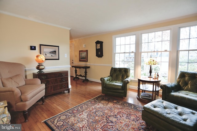 living area featuring hardwood / wood-style flooring, baseboards, and crown molding