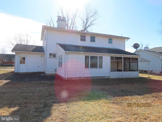 back of house featuring a sunroom, a chimney, and a lawn