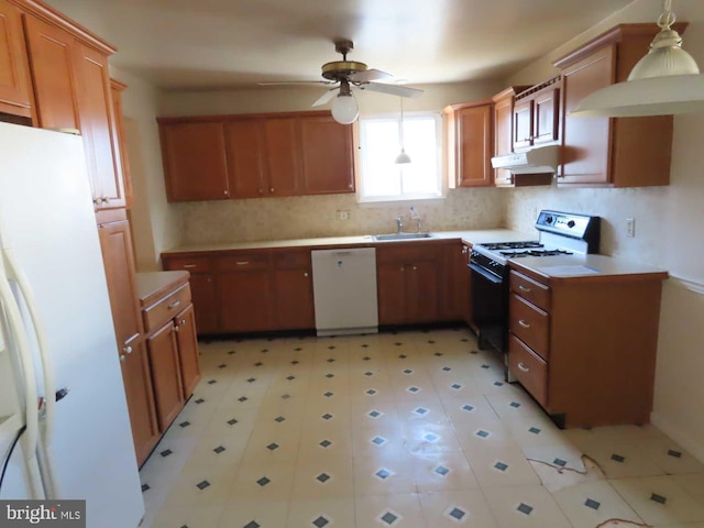 kitchen featuring white appliances, under cabinet range hood, brown cabinetry, and a sink