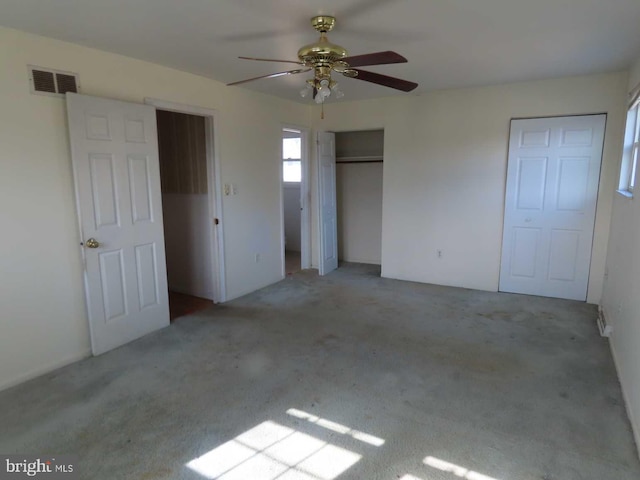 unfurnished bedroom with carpet, visible vents, ceiling fan, and two closets