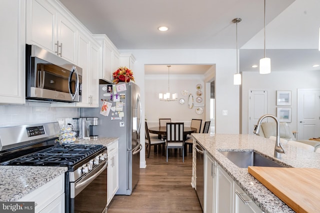 kitchen with stainless steel appliances, wood finished floors, a sink, white cabinets, and decorative backsplash