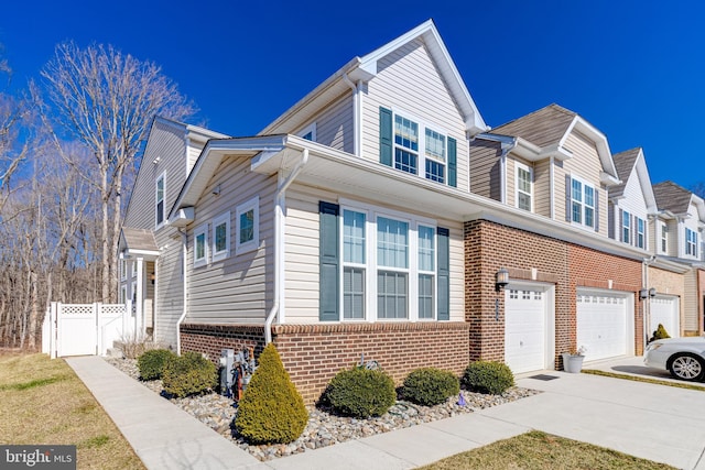 view of property featuring a garage, brick siding, fence, concrete driveway, and a gate