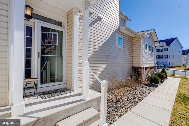 view of exterior entry featuring a porch, a residential view, and brick siding