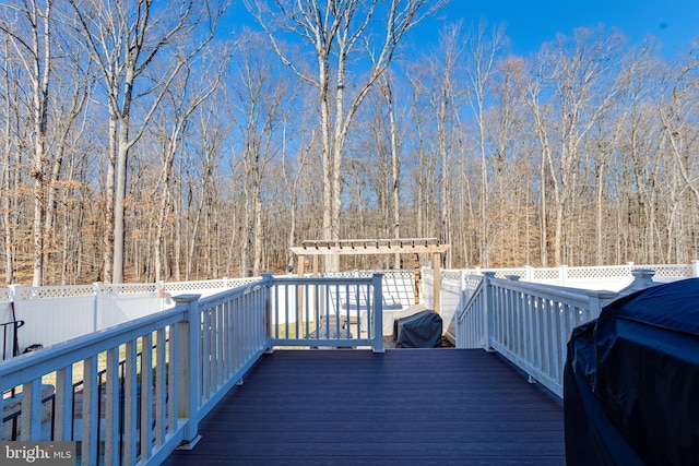 wooden terrace with fence, grilling area, and a view of trees