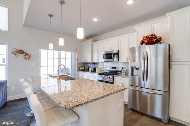 kitchen with tasteful backsplash, white cabinets, a kitchen island with sink, stainless steel appliances, and a sink