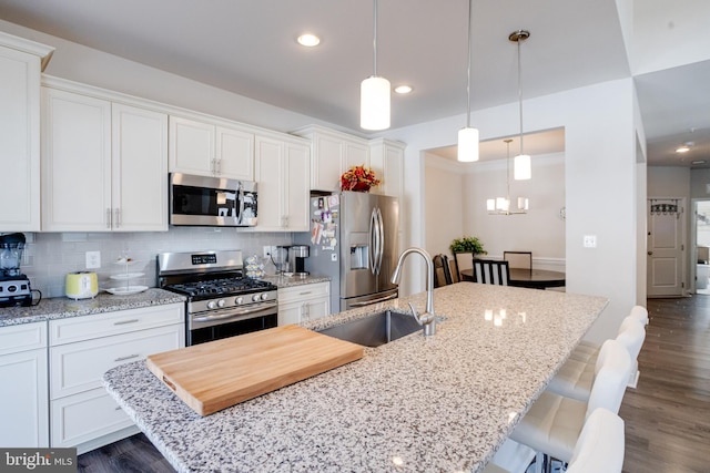 kitchen featuring a kitchen island with sink, stainless steel appliances, dark wood-type flooring, a sink, and tasteful backsplash