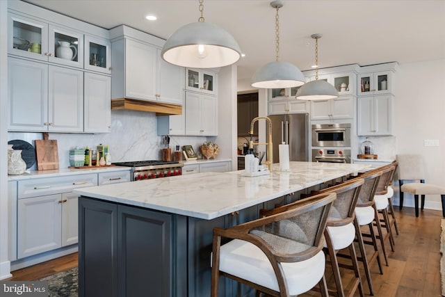 kitchen featuring stainless steel appliances, dark wood-style flooring, decorative backsplash, an island with sink, and decorative light fixtures