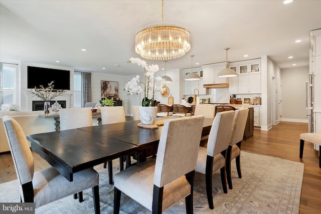 dining area featuring recessed lighting, light wood-type flooring, a fireplace, and a notable chandelier