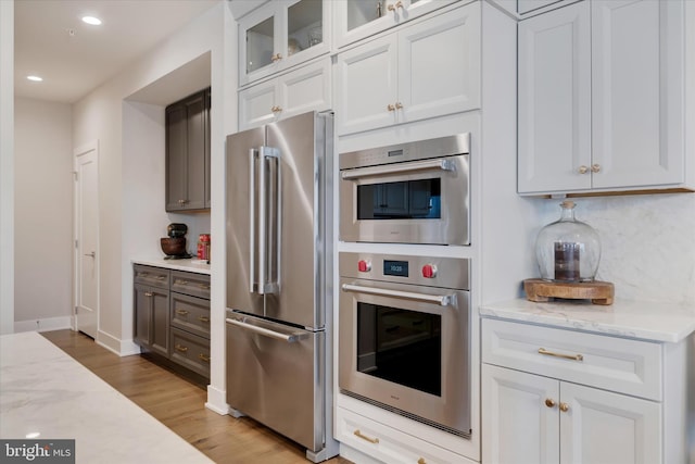 kitchen with recessed lighting, white cabinetry, appliances with stainless steel finishes, light wood finished floors, and glass insert cabinets