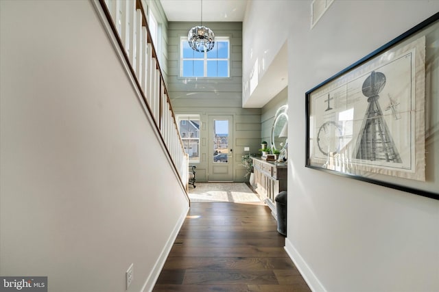 foyer with baseboards, a towering ceiling, hardwood / wood-style floors, stairs, and a notable chandelier