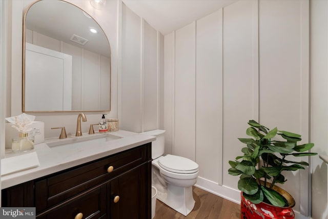 bathroom featuring visible vents, toilet, wood finished floors, vanity, and a decorative wall