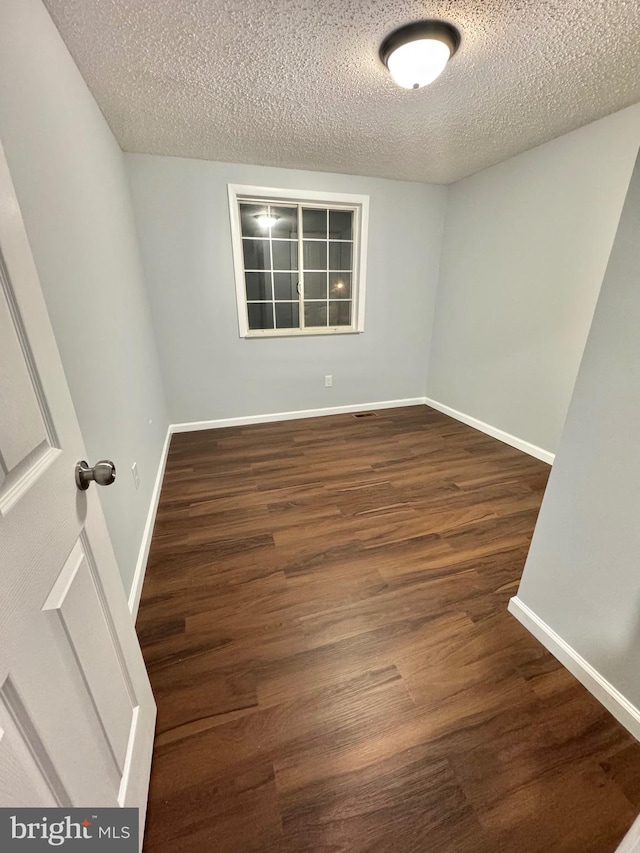 unfurnished room with a textured ceiling, wood finished floors, and baseboards