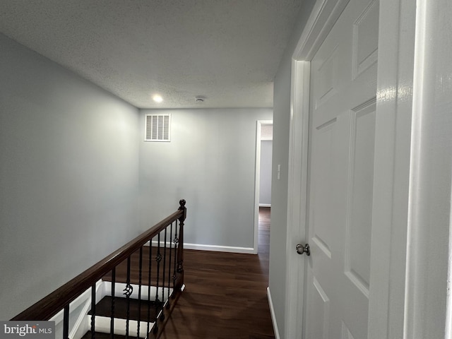 hall with a textured ceiling, dark wood-type flooring, an upstairs landing, visible vents, and baseboards