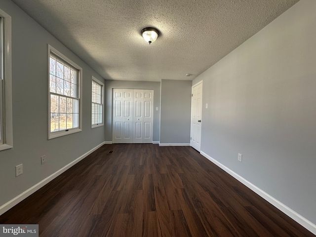 unfurnished bedroom with a textured ceiling, a closet, dark wood finished floors, and baseboards