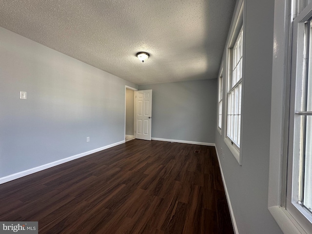 unfurnished room with dark wood-style floors, a textured ceiling, and baseboards