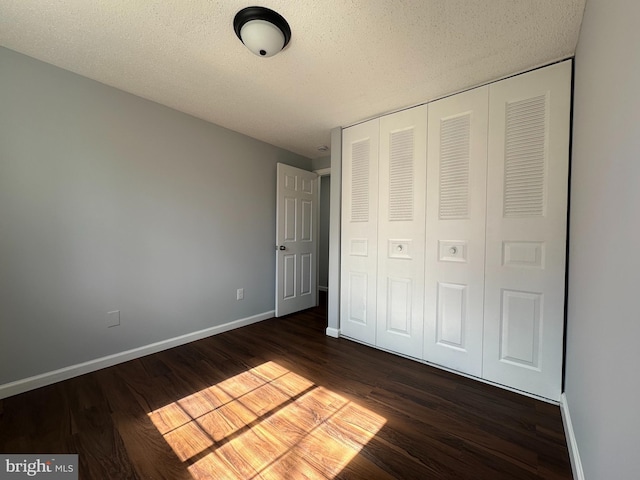 unfurnished bedroom with a textured ceiling, a closet, wood finished floors, and baseboards