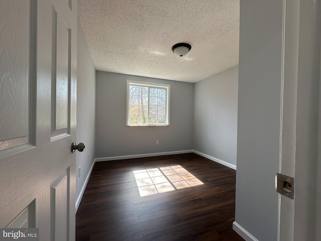 spare room with baseboards, dark wood finished floors, and a textured ceiling