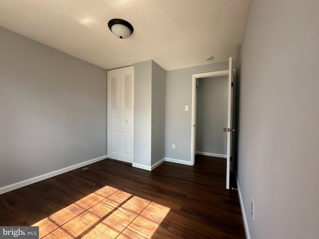 unfurnished bedroom with a textured ceiling, dark wood-style flooring, and baseboards