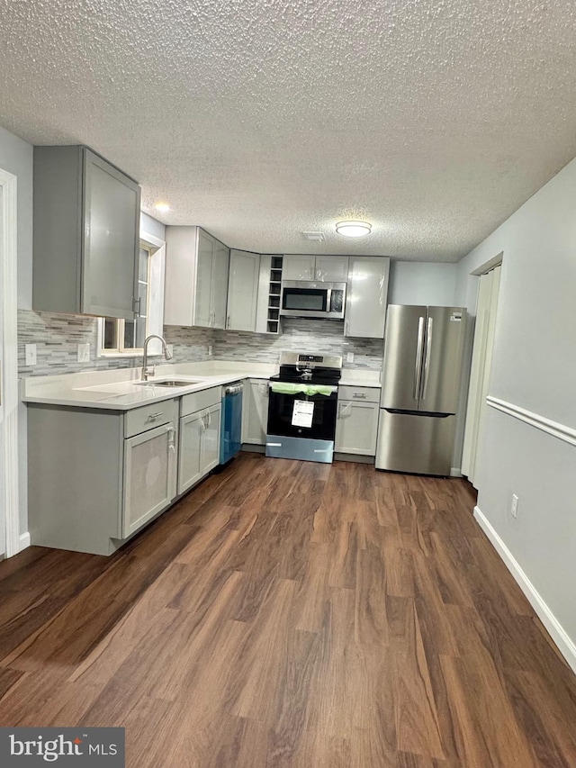 kitchen featuring gray cabinets, light countertops, appliances with stainless steel finishes, dark wood-type flooring, and a sink