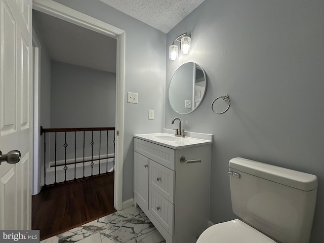 bathroom with a textured ceiling, toilet, vanity, baseboards, and marble finish floor