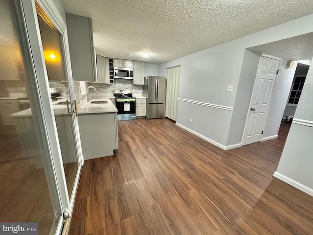 kitchen with dark wood finished floors, stainless steel appliances, tasteful backsplash, light countertops, and a sink