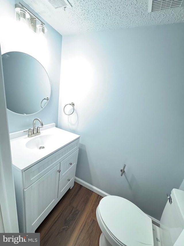 bathroom with a textured ceiling, toilet, wood finished floors, vanity, and baseboards