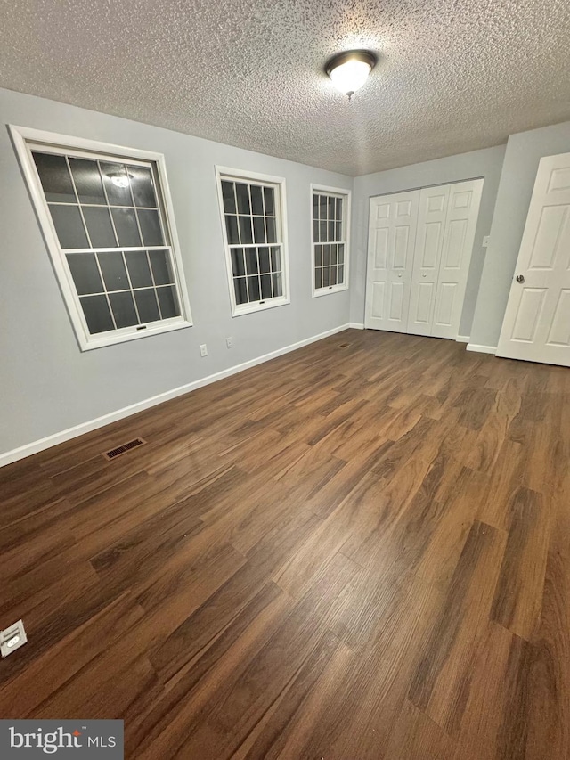 empty room with visible vents, dark wood finished floors, a textured ceiling, and baseboards