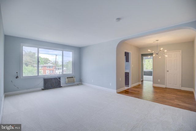 unfurnished room featuring carpet floors, arched walkways, a notable chandelier, radiator, and baseboards