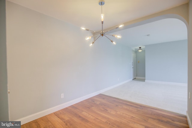 empty room with light wood-type flooring, baseboards, and arched walkways