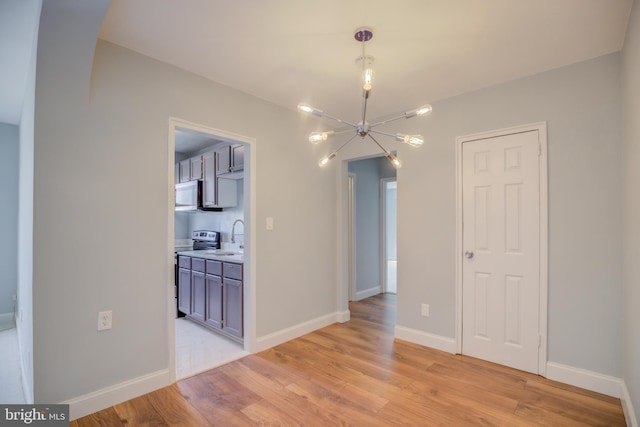 unfurnished dining area with a chandelier, baseboards, a sink, and light wood finished floors