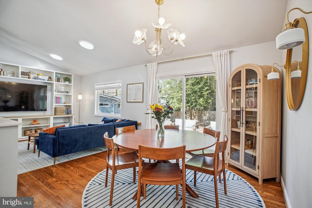 dining space with a wealth of natural light, vaulted ceiling, an inviting chandelier, and wood finished floors