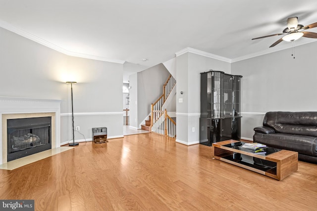 living area featuring wood finished floors, baseboards, a fireplace with flush hearth, ornamental molding, and stairs