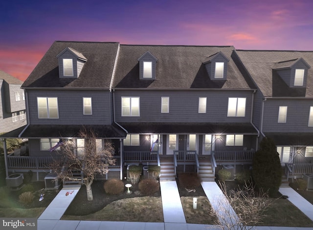 townhome / multi-family property with central air condition unit, a shingled roof, and a porch