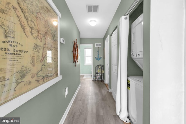 corridor featuring stacked washing maching and dryer, wood finished floors, visible vents, and baseboards