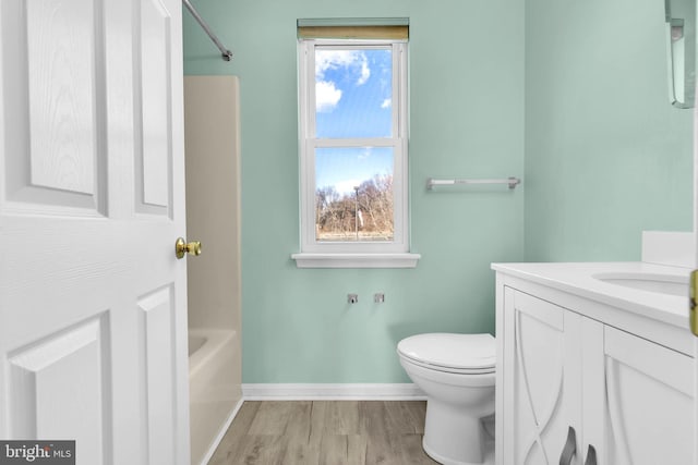 full bathroom with toilet, a bathing tub, vanity, wood finished floors, and baseboards