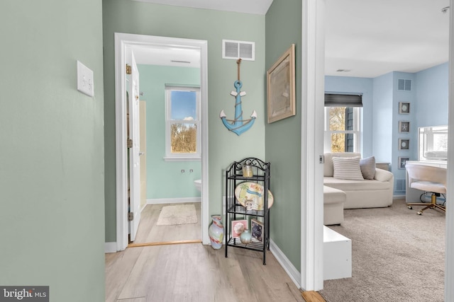 hallway with wood finished floors, visible vents, and baseboards