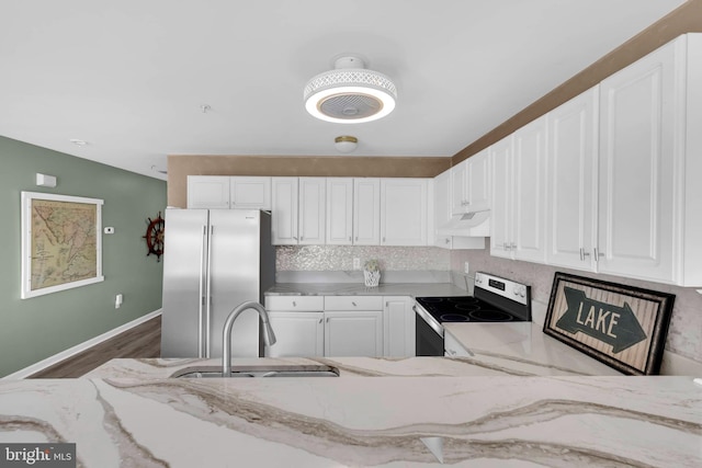 kitchen featuring light stone counters, under cabinet range hood, electric range, a sink, and freestanding refrigerator