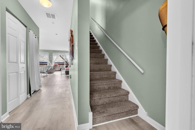 stairs with wood finished floors, visible vents, and baseboards