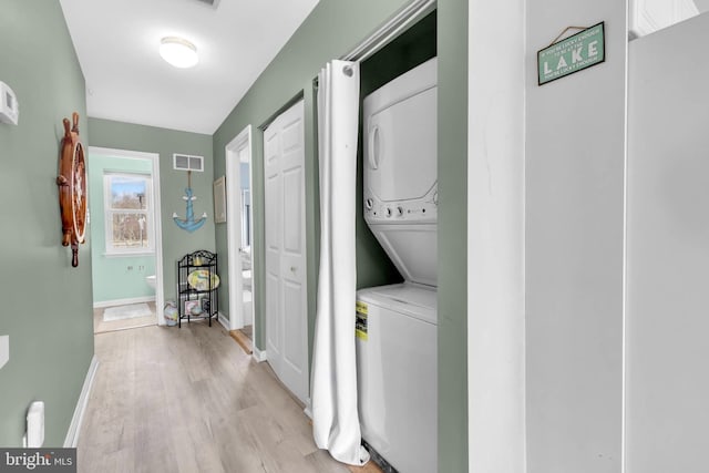 laundry area featuring laundry area, visible vents, baseboards, stacked washer and clothes dryer, and light wood-type flooring