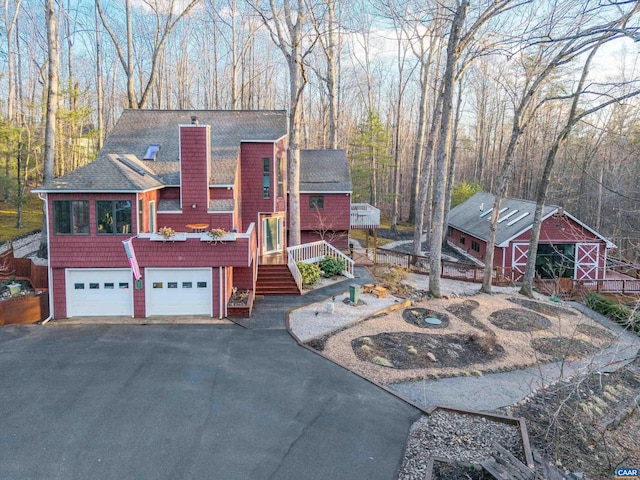 view of front facade featuring driveway, a garage, a barn, a chimney, and an outdoor structure