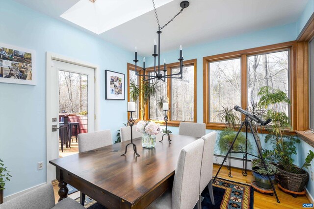 dining room featuring a skylight, a healthy amount of sunlight, baseboard heating, and wood finished floors