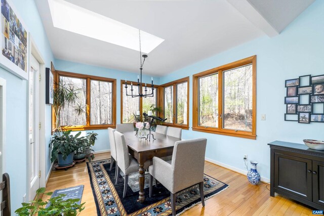 dining area featuring light wood-style floors, a skylight, baseboards, and an inviting chandelier