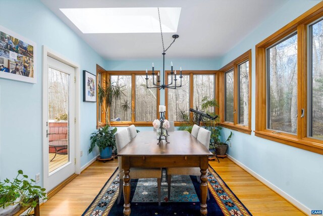 dining space with light wood-type flooring, a skylight, a notable chandelier, and baseboards