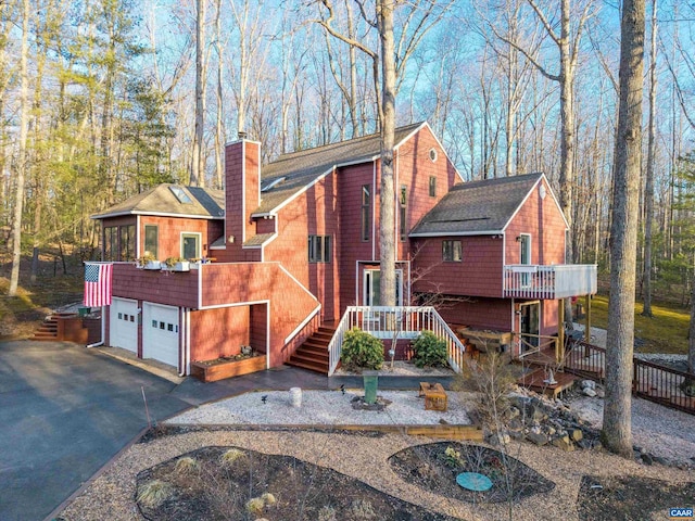 chalet / cabin featuring a deck, aphalt driveway, a garage, stairs, and a chimney