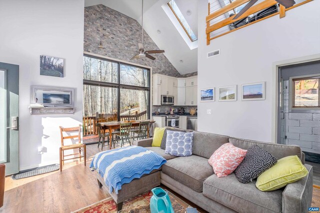 living room with a skylight, visible vents, a ceiling fan, wood finished floors, and high vaulted ceiling